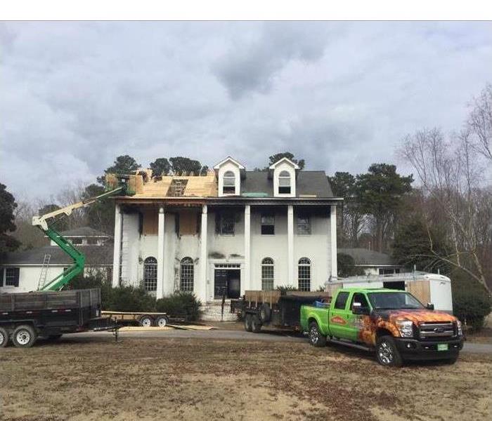 Image of SERVPRO trucks parked in front of a fire damaged home and professionals replacing the roof of this home. 