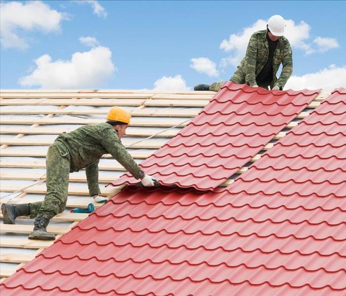 Image of 2 workers fixing the roof of a building. 